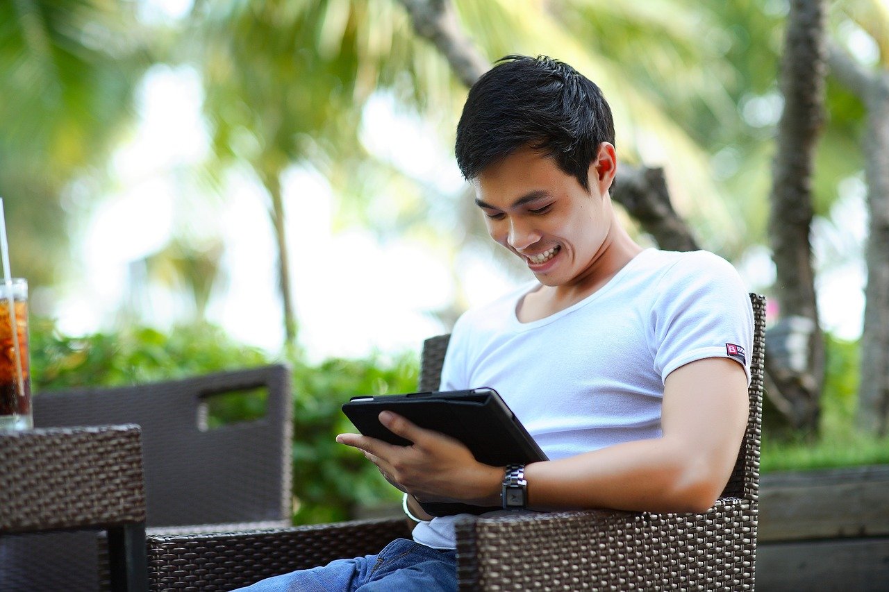 A young man in a white shirt browsing a website with a smile.
